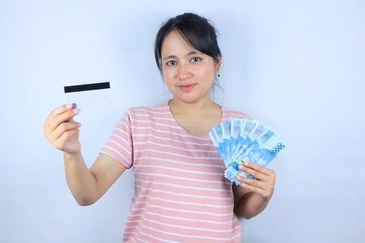 Portrait of a smiling asian young woman holding cash rupiah and credit card on white background photo