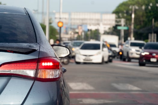 Rear side of grey car with turn on brake light. On body of car with drop of water after rainy. Traffic on the asphalt road many cars in the opposit of crossroads road. photo