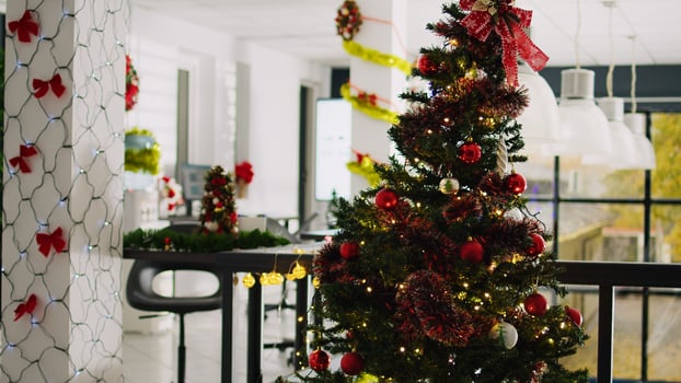 Dolly out shot of empty festive ornate modern office workspace with beautifully decorated Christmas tree. Finance graphs on computer screen in xmas adorn workplace during winter holiday season photo
