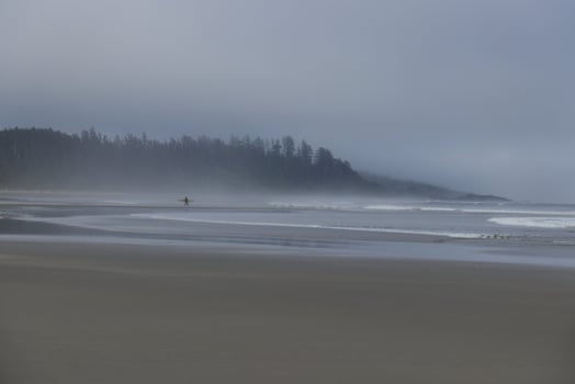 Surfer is walking with a White board along the Long Beach near Tofino, Vancouver Island, Canada at foggy morning photo