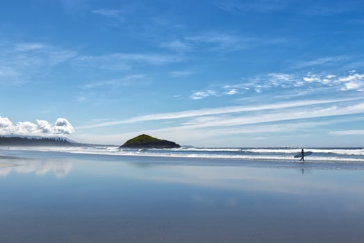 Surfer is walking with a White board along the Long Beach near Tofino, Vancouver Island, Canada at sunny day photo