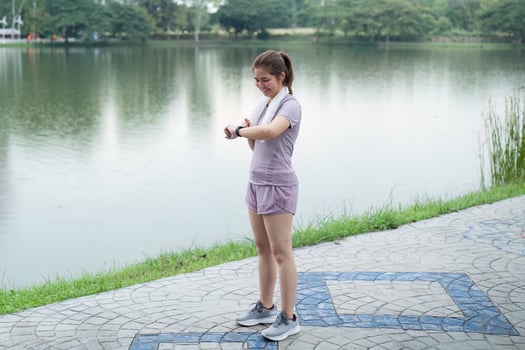 Happy young woman checking her run time on her smart watch after morning run at running park photo