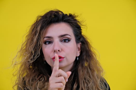 Close-up portrait beautiful girl on a yellow background. woman showing finger silence, girl showing shh sign keep secret photo