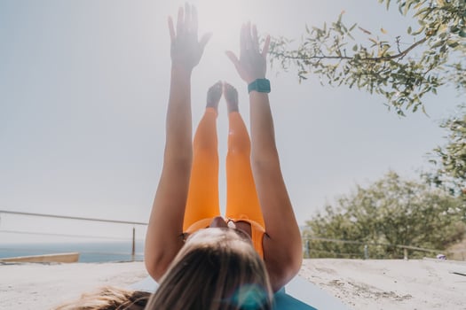 Fitness woman sea. Happy middle aged woman in orange sportswear exercises morning outdoors on yoga mat with laptop in park over ocean beach. Female fitness pilates yoga routine. Healthy lifestyle. photo