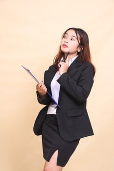 Beautiful formal Asian executive mature woman in suit thinking standing and pose carrying pen clipboard, 3 by 4 body portrait on yellow background for commercial, vacancy and business photo
