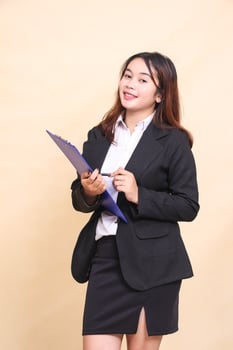 Beautiful formal Asian executive mature woman in suit cheerful smile standing and pose holding clipboard pen to camera, 3 by 4 body portrait on yellow background for commercial, vacancy and business photo