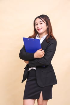 Beautiful formal Asian executive mature woman in suit smile standing and pose holding clipboard pen to camera, 3 by 4 body portrait on yellow background for commercial, vacancy and business photo