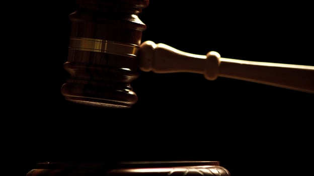 A close-up, dramatic shot of a judge's gavel poised above a sound block, illuminated against a dark background. photo