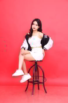 Beautiful young Asian woman wearing elegant sunglasses, hands holding her waist, sitting on a chair wearing a black and white jacket photo