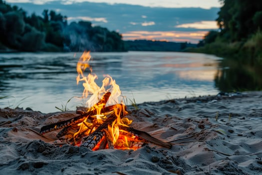 A campfire glowing on a sandy shore beside water photo