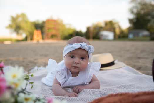 a newborn child lies on a blanket, on the shore. flowers lie nearby. photo