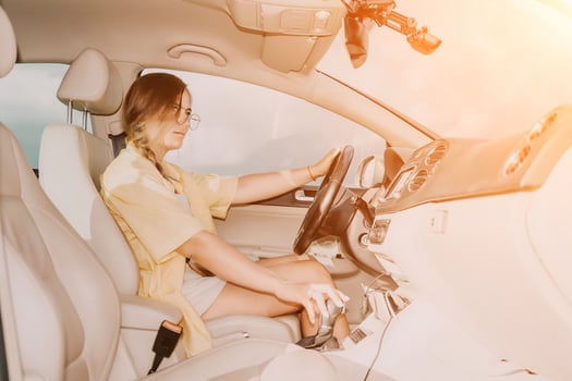 A woman in a yellow shirt is driving a car. She is wearing glasses and has her hands on the steering wheel photo
