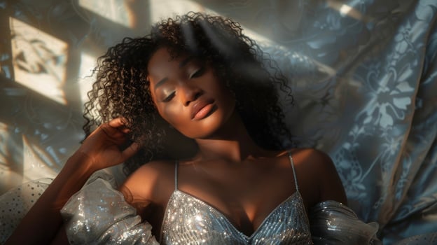 A stunning portrait of a black woman in a shimmering silver dress her dark curls cascading down her back. As the light catches her dress she exudes a powerful and regal aura embodying photo