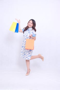 full body Beautiful cheerful Asian woman wearing modern chinese dress shopping promotional paper bag orange and above isolated on white background. happy Chinese New Year photo
