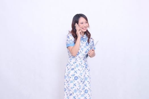 beautiful cheerful Indonesian Chinese woman looking sideways top left wearing modern Chinese blue dress holding tablet holding phone isolated white background photo