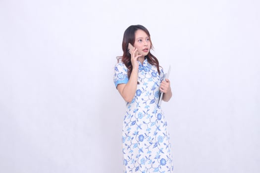 beautiful Indonesian Chinese woman looking sideways top left wearing modern Chinese blue dress holding tablet holding phone isolated white background photo