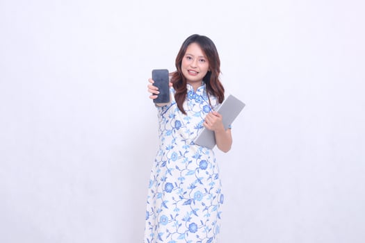 beautiful asian woman wearing blue chinese dress front view flat smile holding tablet and looking at cellphone screen isolated white background photo