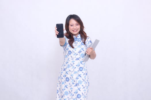 beautiful asian girl wearing blue chinese dress front view happy smile holding tablet and looking at cell phone screen isolated white background photo