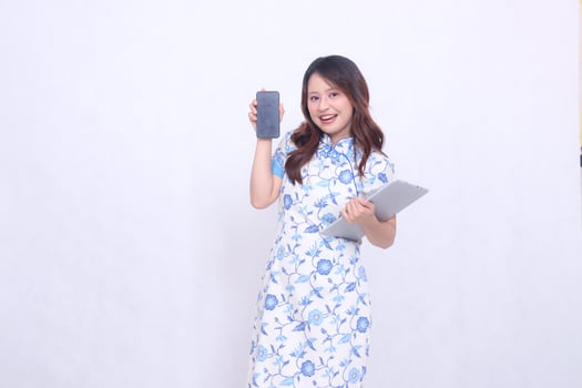 beautiful asian girl wearing blue chinese dress cheerful smile holding tablet and looking at cell phone screen isolated white background photo