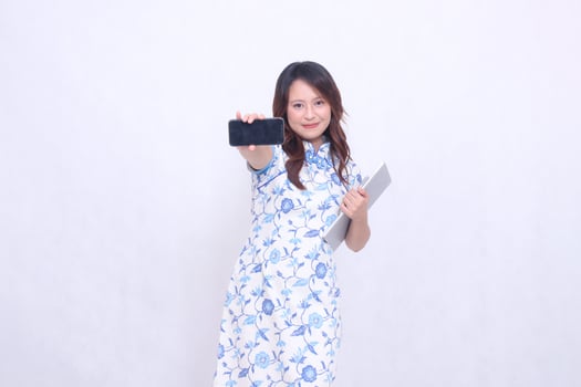beautiful asian woman wearing blue chinese dress front view small smile holding tablet and looking at cellphone screen isolated white background photo