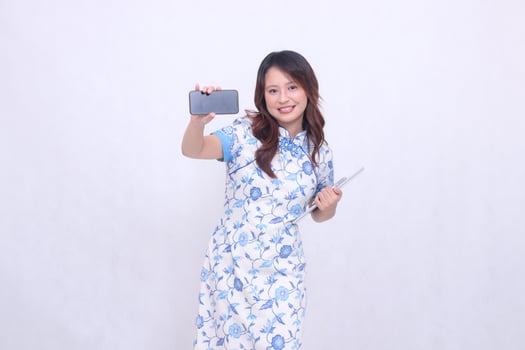 beautiful asian girl wearing blue chinese dress front view big smile holding tablet and looking at cellphone screen isolated white background photo