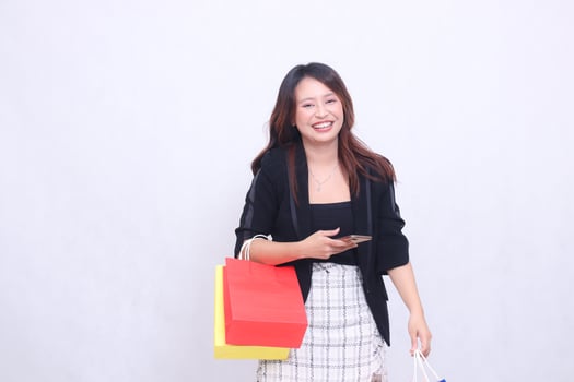Young beautiful woman customer in her 20s formal office laughing while carrying cellphone carrying shopping paper bag isolated on white background photo