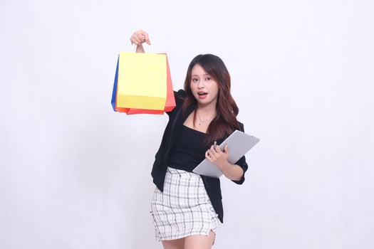 young beautiful woman customer 20s formal office smile surprised look at camera hold pen tablet and carry shopping paper bag up high isolated white background photo