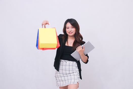 young beautiful woman customer 20s formal office smile look at camera hold tablet pen and lift shopping paper bag up high isolated white background photo