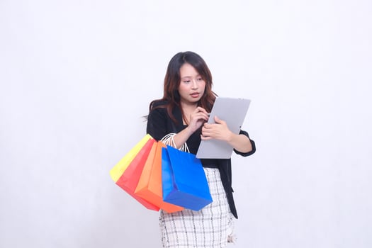 young beautiful woman customer 20s formal serious office holding pen cross checking order on tablet looking ahead and carrying shopping paper bag isolated white background photo