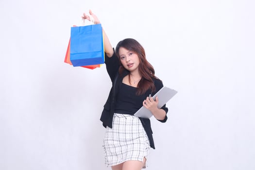 young beautiful girl customer 20s formal office flat smile tilted hold tablet pen and carry shopping paper bag upwards isolated white background photo