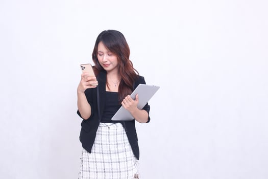 beautiful southeast asian woman 20s formal office smile looking at cellphone and carrying tablet for promo isolated white background photo