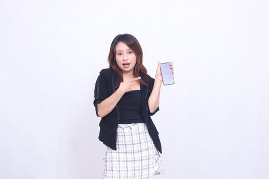 beautiful Indonesian office woman 20s expression of surprise on promotion of cellphone gadget screen for promo while pointing at it underneath isolated white background photo