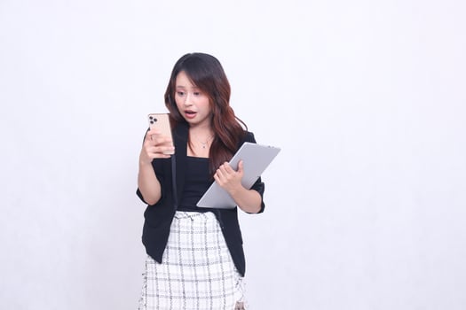 beautiful southeast asian girl 20s formal office shocked looking at cellphone and carrying tablet for promo isolated white background photo
