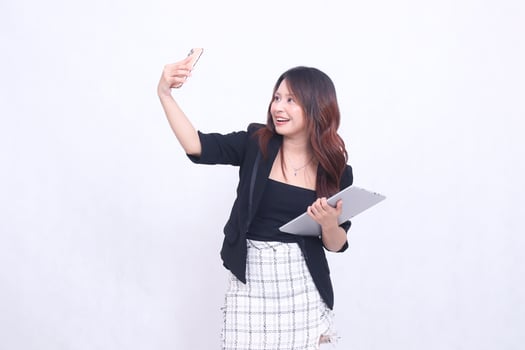 Beautiful Southeast Asian girl in her 20s, formal office, cheerful smile, making a call in front of the camera, carrying a tablet for promo, isolated on a white background photo