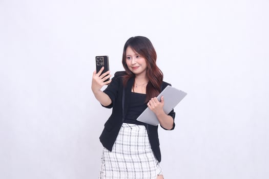 beautiful Indonesian woman 20s formal office smile call via black cellphone gadget candid and bring tablet for promo isolated white background photo