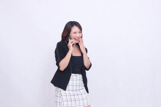 the charm of a beautiful Asian office woman in her 20s, laughing expression while making a phone call on a cell phone gadget while covering her mouth isolated on a white background photo