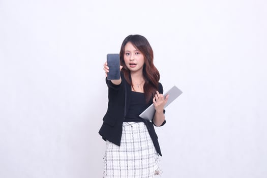 beautiful southeast asian woman 20s formal office smiling dumbfounded looking at cellphone gadget screen and carrying tablet for promo isolated white background photo