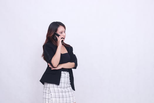 the charm of a beautiful Asian office woman in her 20s flat expression is on the phone using a cellphone gadget for promos while holding her arms to the left isolated on a white background photo