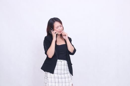 the charm of a beautiful Asian office woman in her 20s with a bitter expression while making a phone call on a cell phone while holding her hand to her mouth isolated on a white background photo