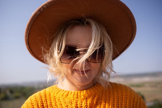 A woman wearing a brown hat and sunglasses is smiling photo