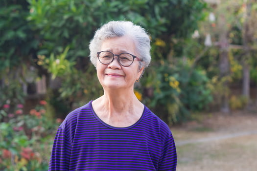 A portrait of an elderly woman wearing eyeglasses, smiling and looking at the camera while standing in a garden. Space for text. Concept of old people and healthcare photo