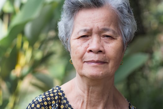 Asain elderly woman smiling and looking at camera while standing in a garden photo