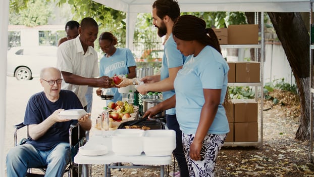 Group dedicated to charity helping out the poor giving away free food including fresh fruits to homeless people. Volunteers give assistance to alleviate hunger for disabled person in wheelchair. photo