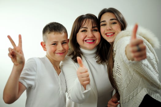 Show thumb class to camera mother white background lifestyle real people concept Family mom son and daughter stand together in white clothes love family positive emotions joy White background studio photo