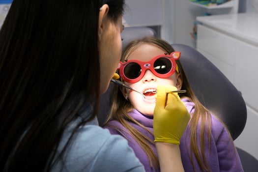 pediatric dentistry close-up little girl opened mouth shows teeth doctor looks at whether she has caries fillings treatment examination by doctor shine in eyes yellow hygienic gloves photo