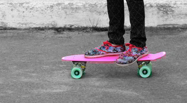 Close up of girl's feet in floral sneakers standing on pink penny board with green wheels photo