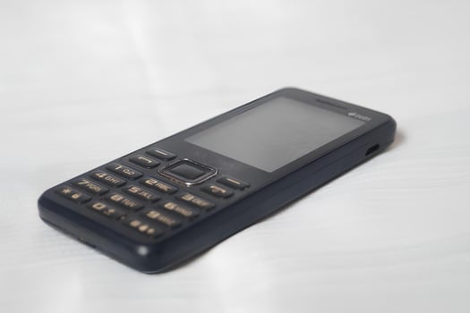 A black flip phone is laying on a white surface photo