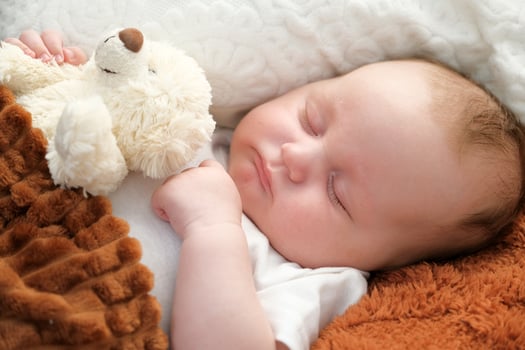 a newborn baby sleeps on a bed. A teddy bear lies nearby. mother and child. photo