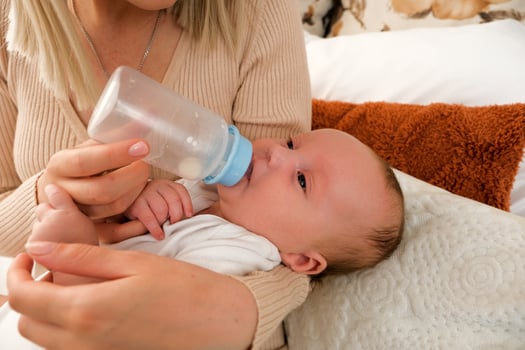 mom feeds a newborn baby with a bottle. the sun is shining in the background. photo