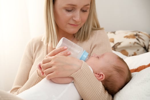 mom feeds a newborn baby with a bottle. the sun is shining in the background. photo